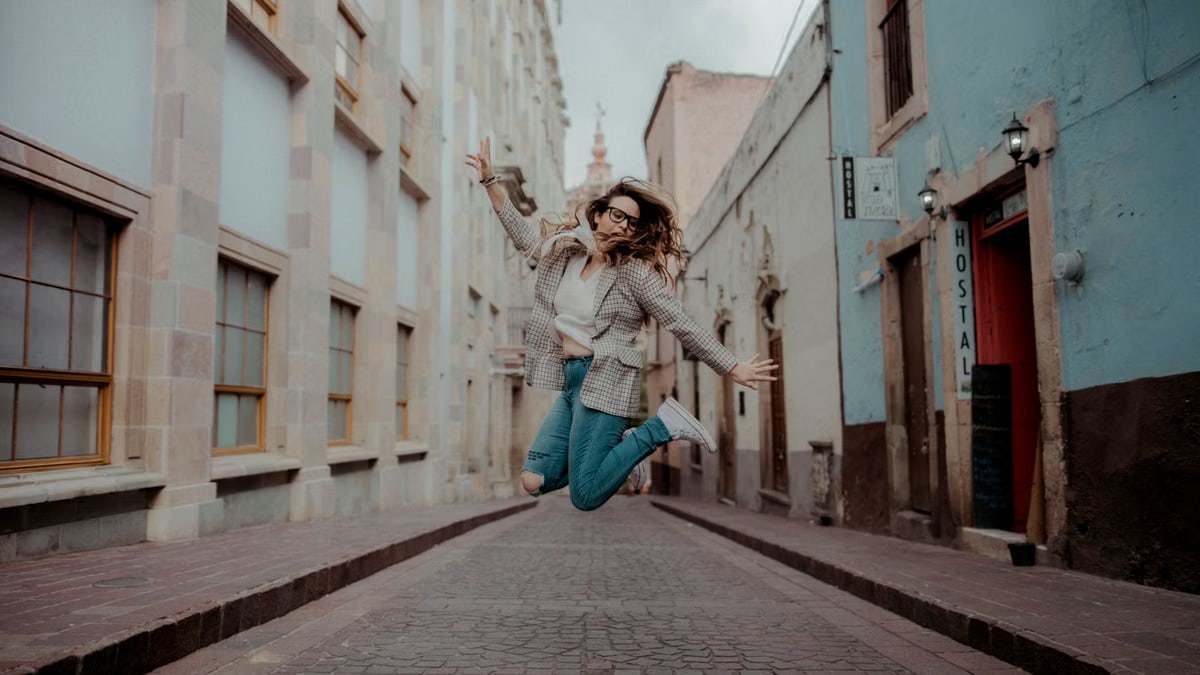 A stylish woman jumps joyfully in a vibrant city street, showcasing urban fashion.